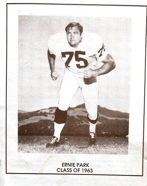 Black-and-white photo of Ernie Park in a football uniform with the number 75, posed in a three-point stance on a field. The image is framed like a yearbook or program page and includes the caption โErnie Park, Class of 1963.โ