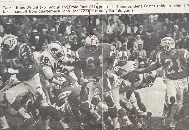 Black-and-white newspaper-style action photo showing Ernie Park, wearing number 61, blocking during a muddy football game, with a caption above identifying him and other players involved in the play.