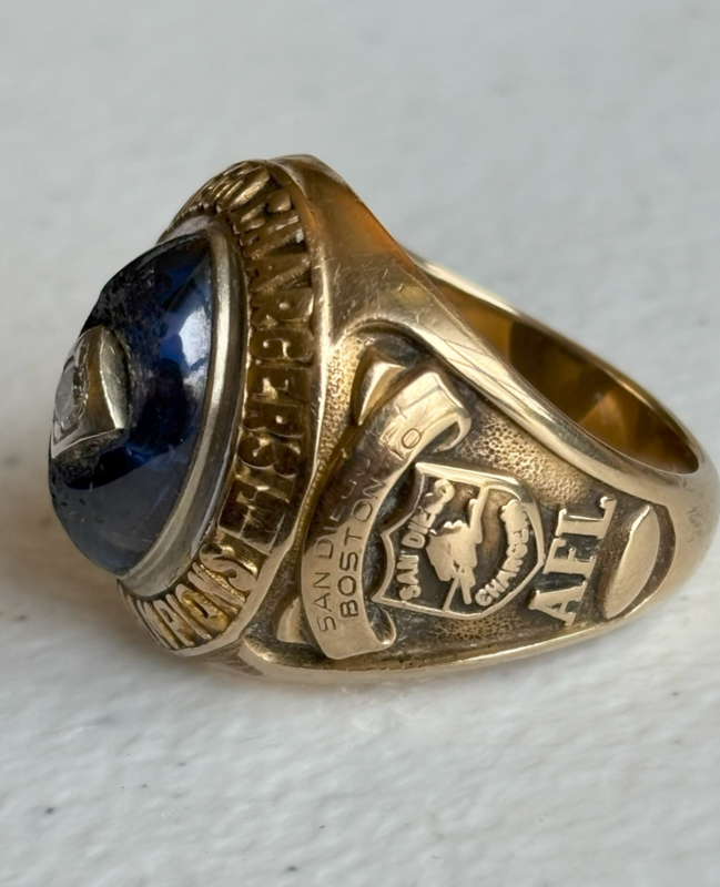 Close-up of a gold championship-style ring with a dark blue stone, engraved with โAFLโ and โSan Diego,โ featuring a football player emblem on the side.