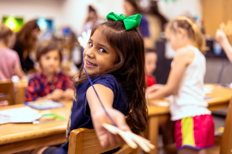 Kindergarten students participate in a classroom activity at tables in the Wylie East Elementary library while staff members assist around the room.