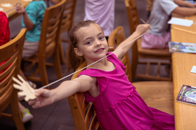 Kindergarten students participate in a classroom activity at tables in the Wylie East Elementary library while staff members assist around the room.