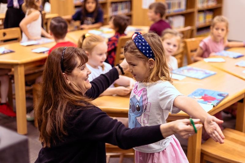 Kindergarten students participate in a classroom activity at tables in the Wylie East Elementary library while staff members assist around the room.