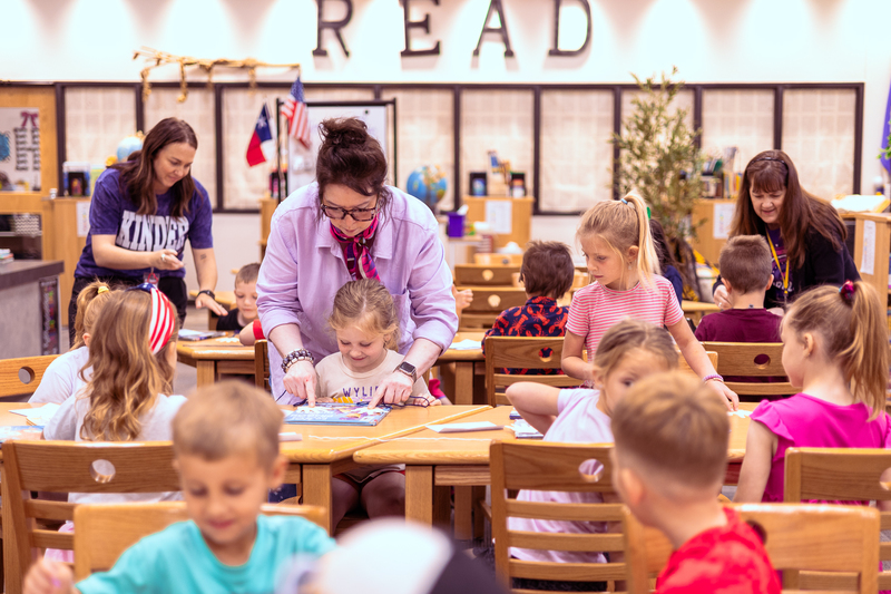 Kindergarten students participate in a classroom activity at tables in the Wylie East Elementary library while staff members assist around the room.