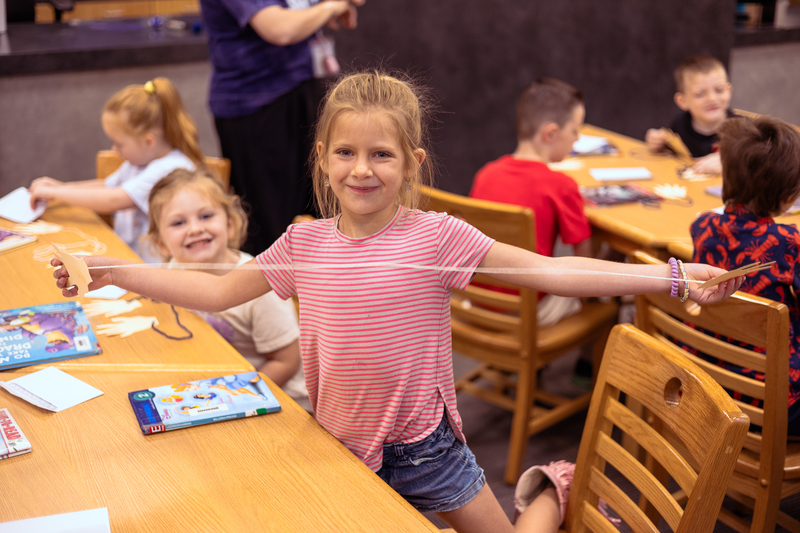 Kindergarten students participate in a classroom activity at tables in the Wylie East Elementary library while staff members assist around the room.