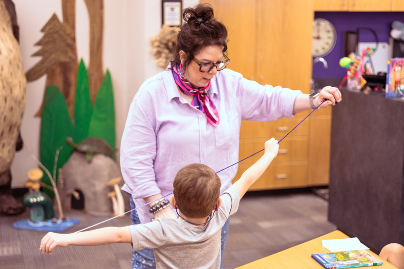 Kindergarten students participate in a classroom activity at tables in the Wylie East Elementary library while staff members assist around the room.