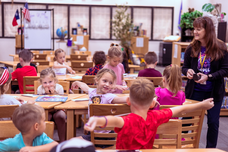Kindergarten students participate in a classroom activity at tables in the Wylie East Elementary library while staff members assist around the room.