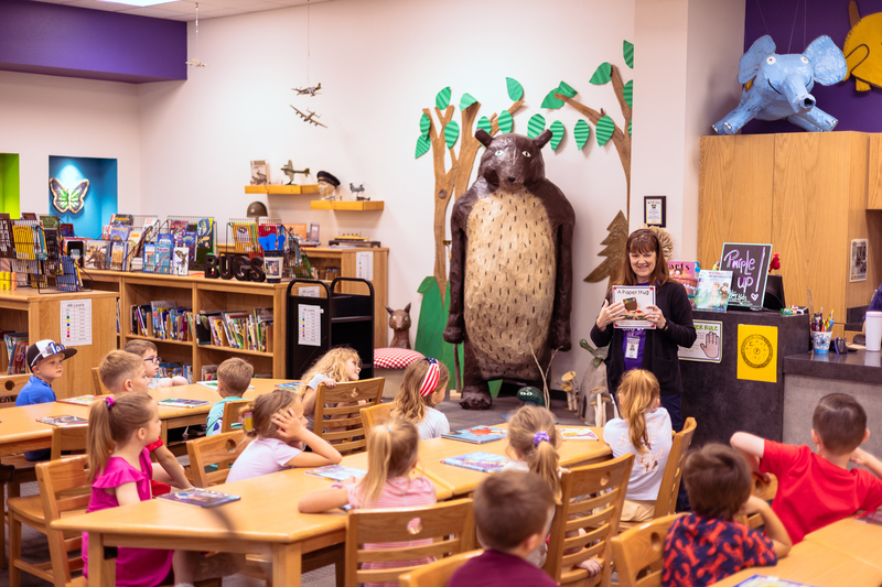 Kindergarten students participate in a classroom activity at tables in the Wylie East Elementary library while staff members assist around the room.