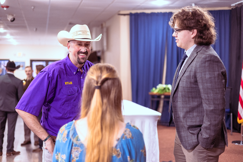 Student seated while a Wylie staff member stands behind in a purple shirt and cowboy hat during the ceremony.