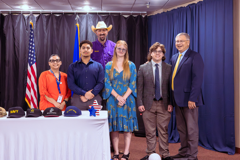 Group of students and adults posing behind a table with military branch hats at Military Signing Day.