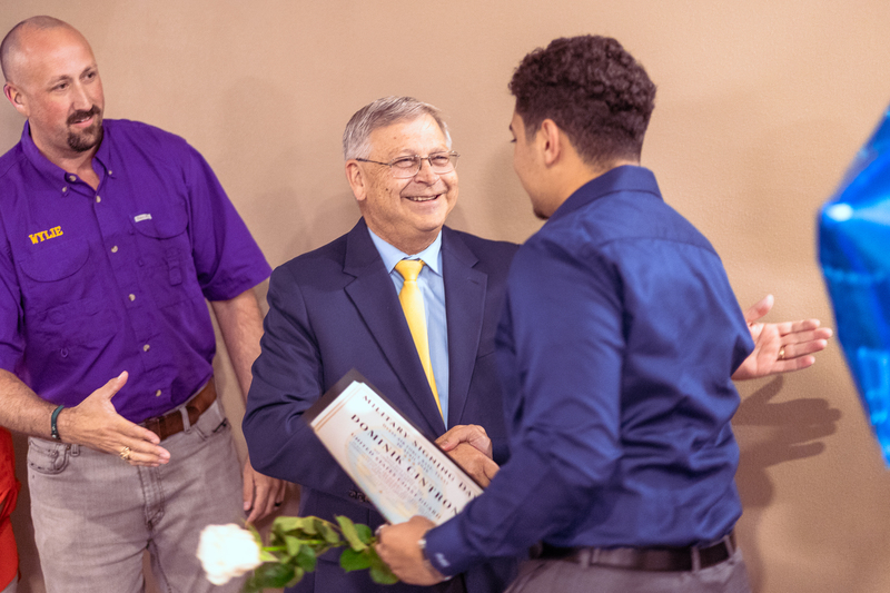 Student shaking hands with a man in a suit during a recognition moment at Military Signing Day.