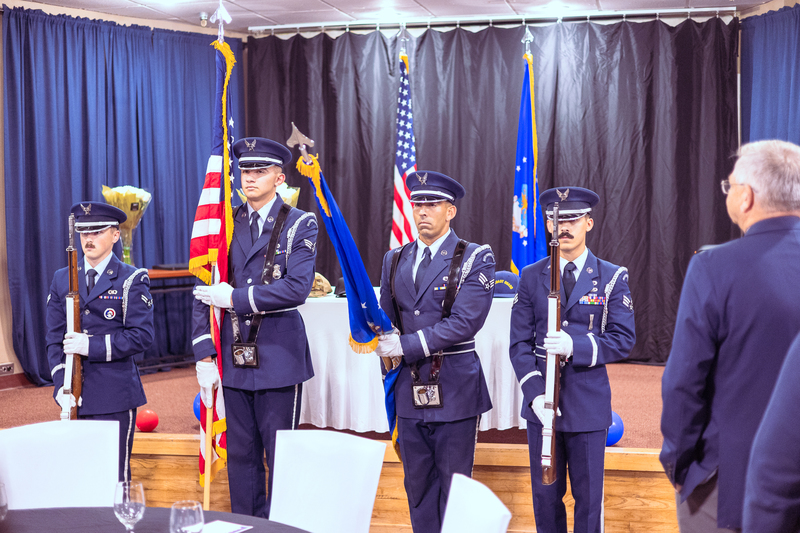 Students standing at the front of the room during the ceremony with military flags behind them.
