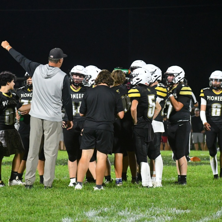 The coaches talk to the football team in a huddle on the field.