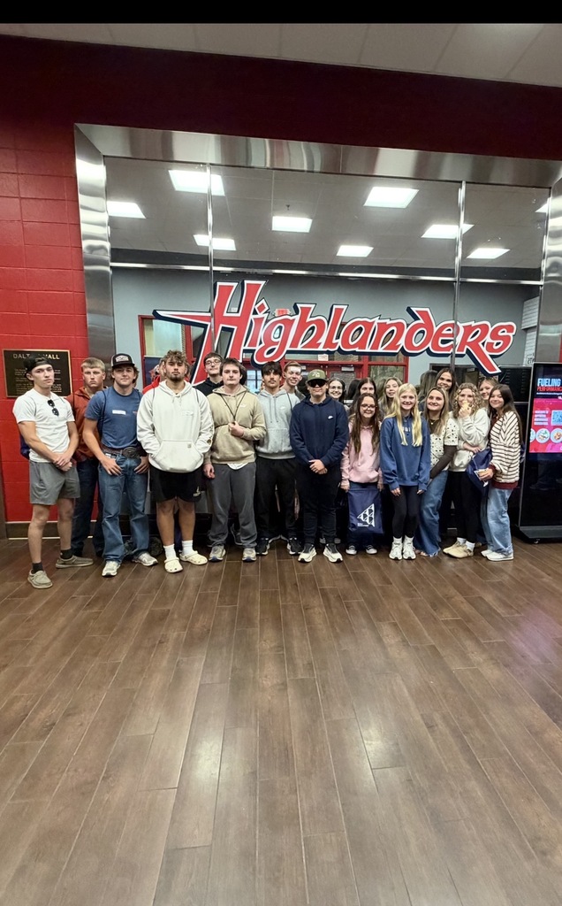20 high school students stand in front of the Highlanders sign outside what appears to be the bookstore!