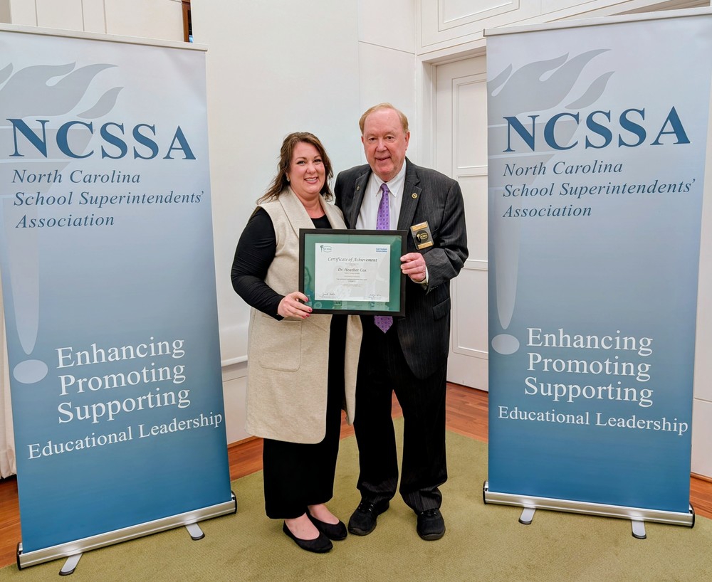 woman and man holding certificate, banners on each side that say "NCSSA north carolina school superintendents' association"