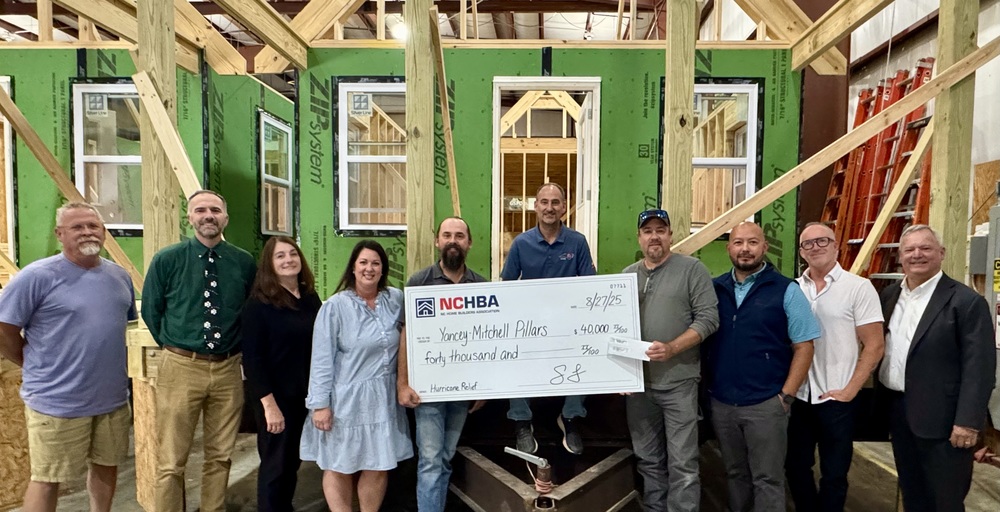 8 men and 2 women holding giant check in front of partially built tiny home