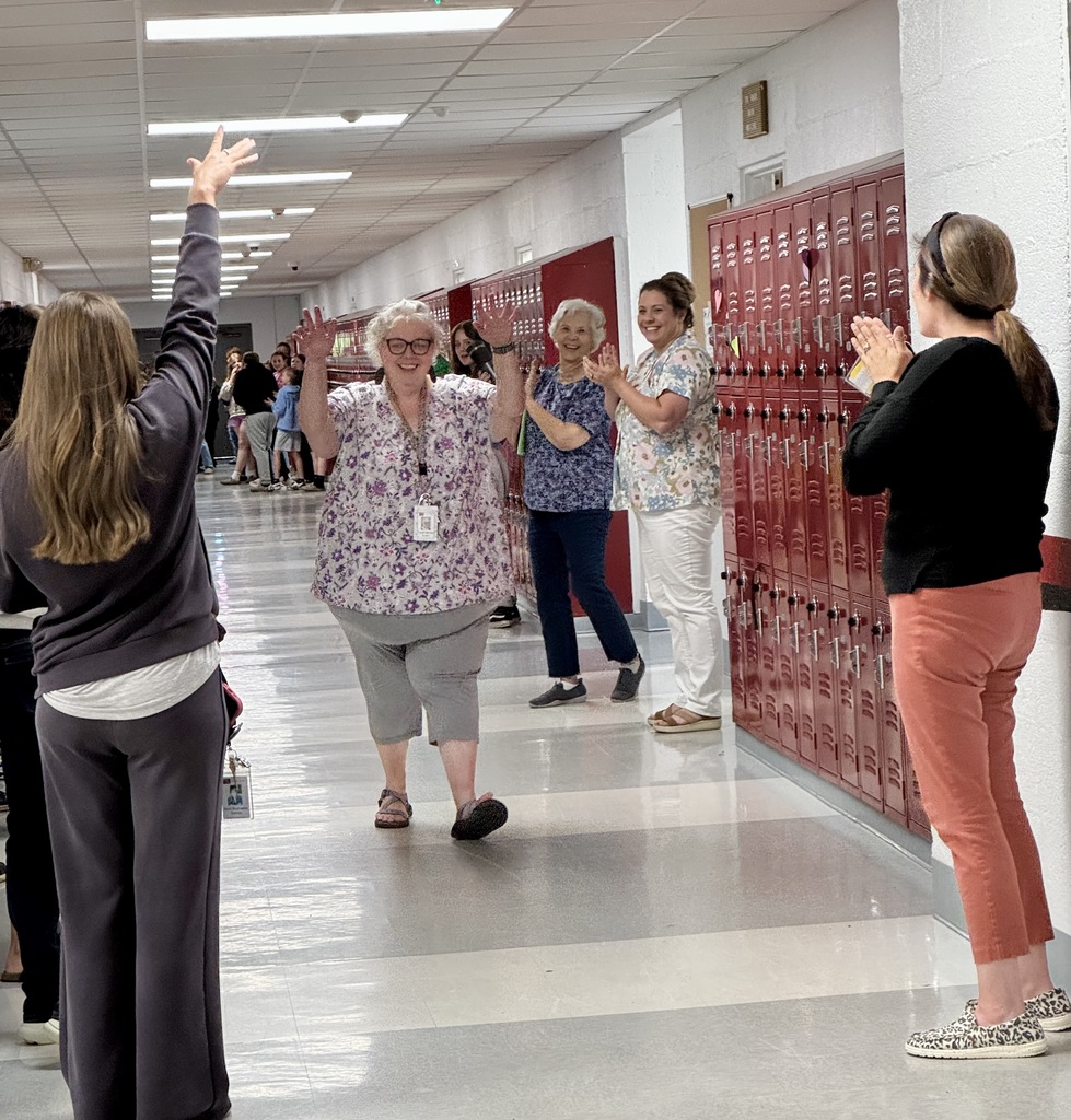 woman walking down a school hallway with people lined on both sides clapping for her