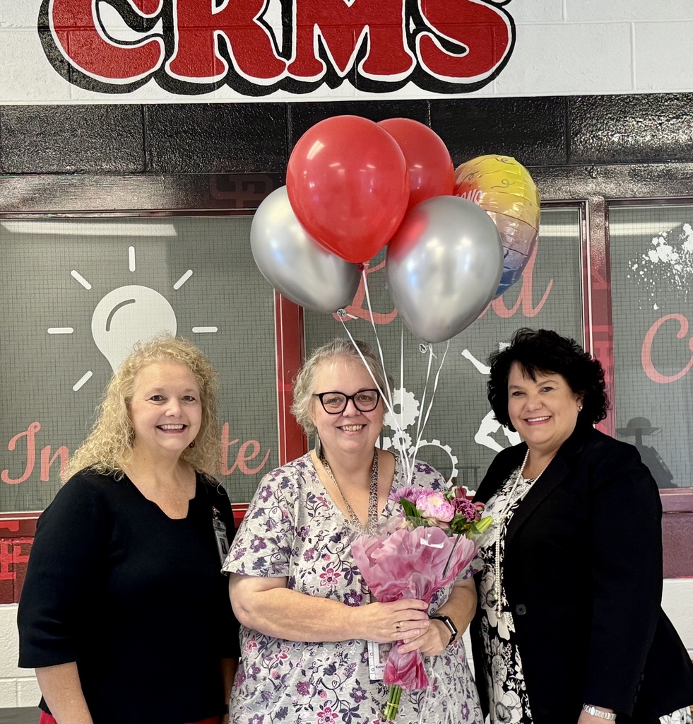 three women smiling, one in the middle holding flowers and balloons