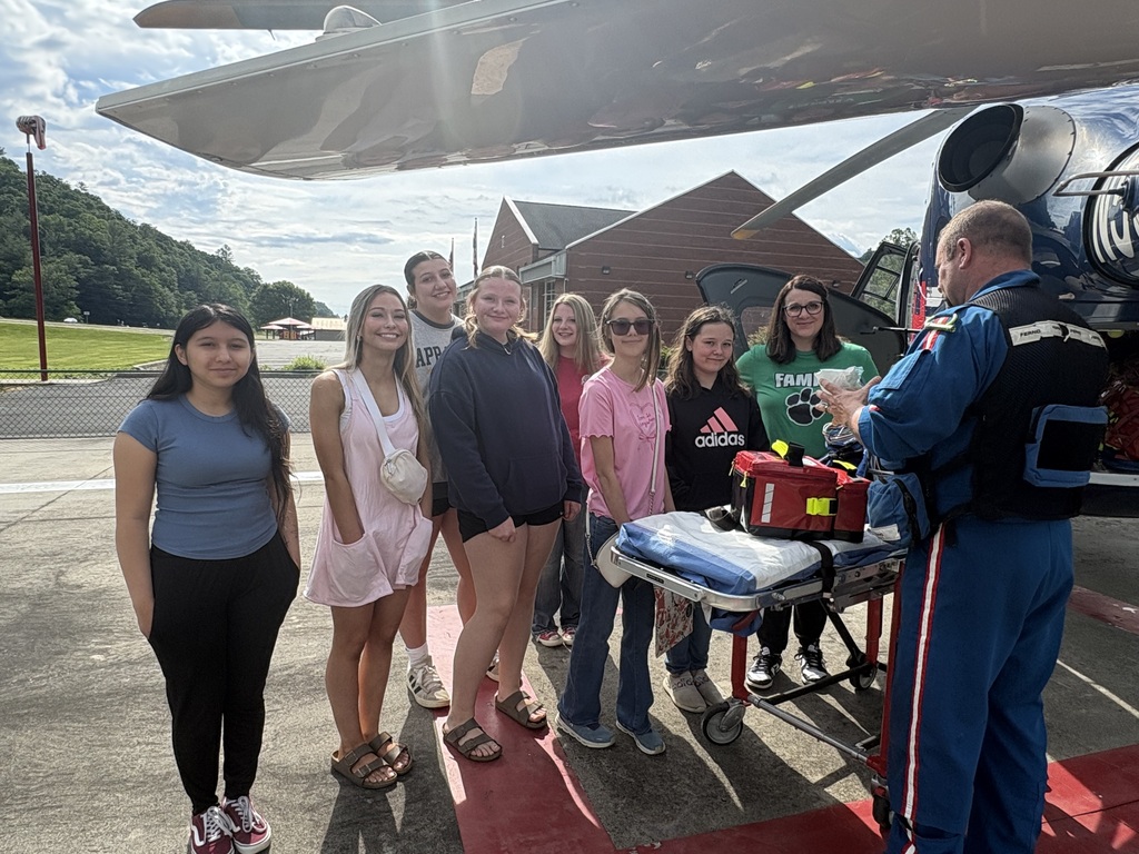 girls standing in front of gurney as medic demonstrates AED device next to a helicopter