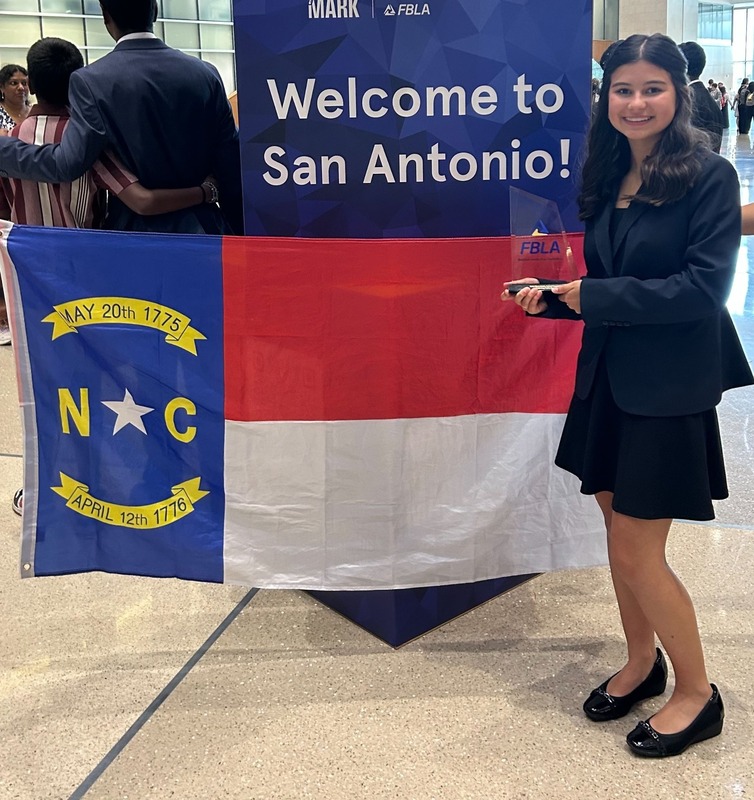 female student in business attire holding a trophy and standing in front of NC flag
