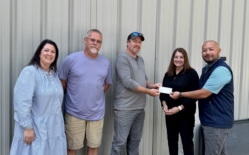 3 men and 2 women posing while holding a check