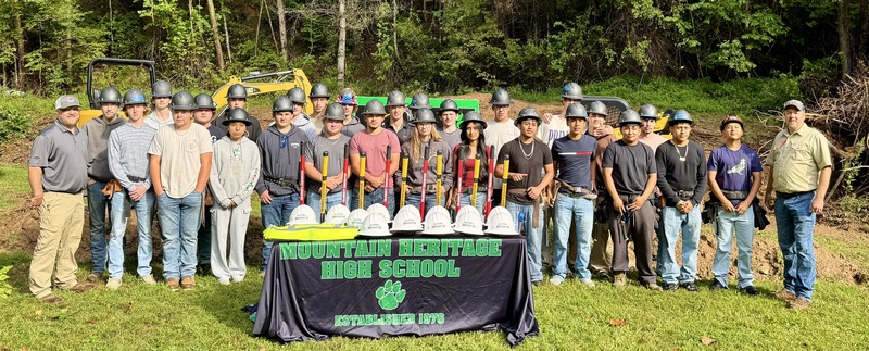 high school students lined up behind table with hard hats and safety vests on it