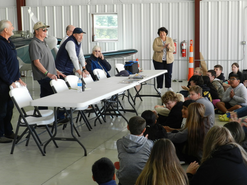 a group of men standing behind a table speaking to a group of students