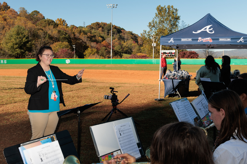 woman directing high school band players on a baseball field