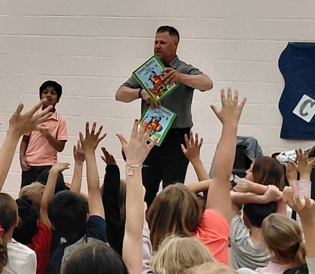 children raising hands as man shows books