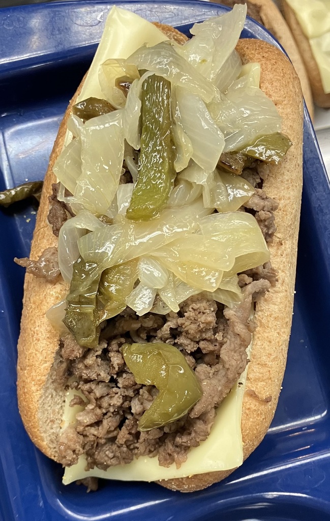 Steak and cheese sandwich on a whole wheat bun, with peppers and onions
