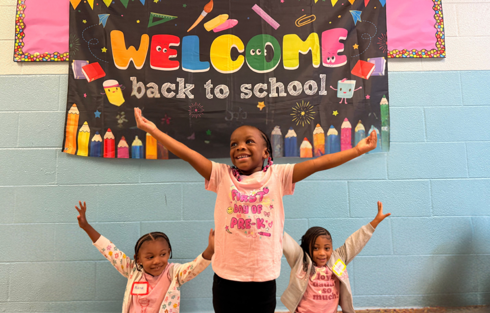 Three young girls raise their arms in the shape of the letter "Y" for the first day of school in Yonkers