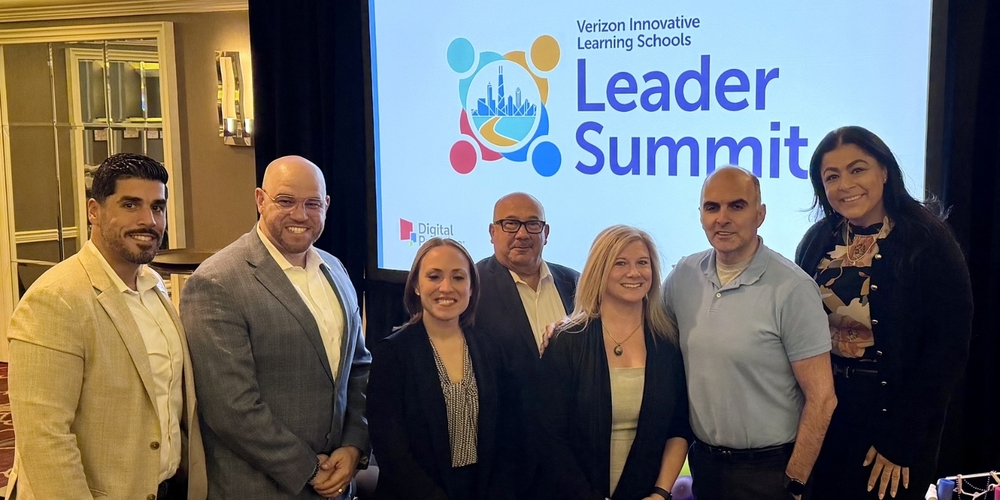 Six educators and school leaders stand together for a group photo at the Verizon Innovative Learning Schools Leader Summit, with the event logo displayed on a screen behind them.