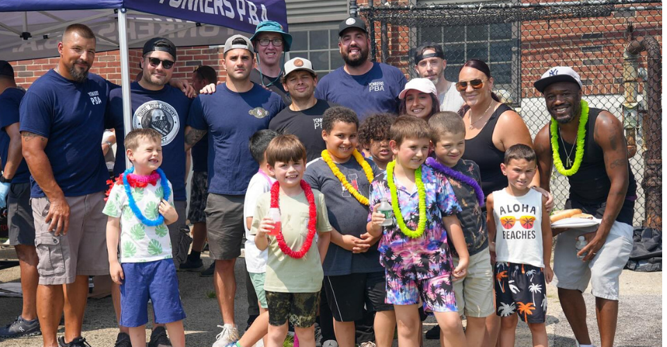 Group of students wearing leis and happy faces surrounded by members of the Yonkers PBA who treated them to a Barbeque