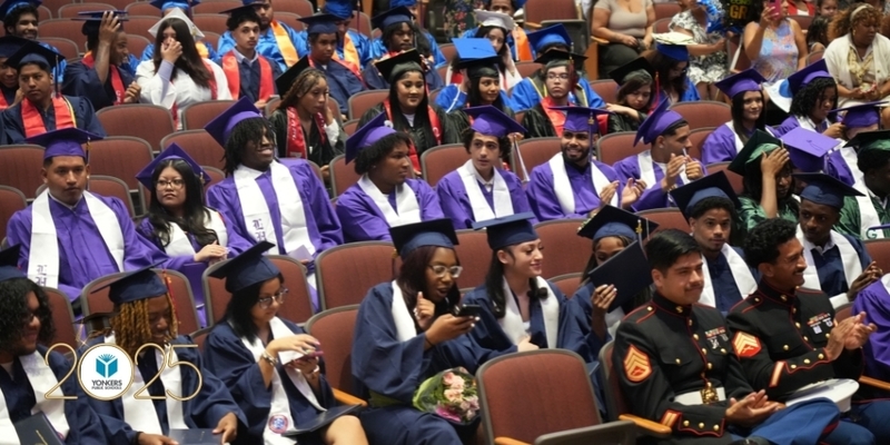 High school graduates sitting in the audiotrium seats during the ceremony. In the front row are two decorated members of the United States Marines.