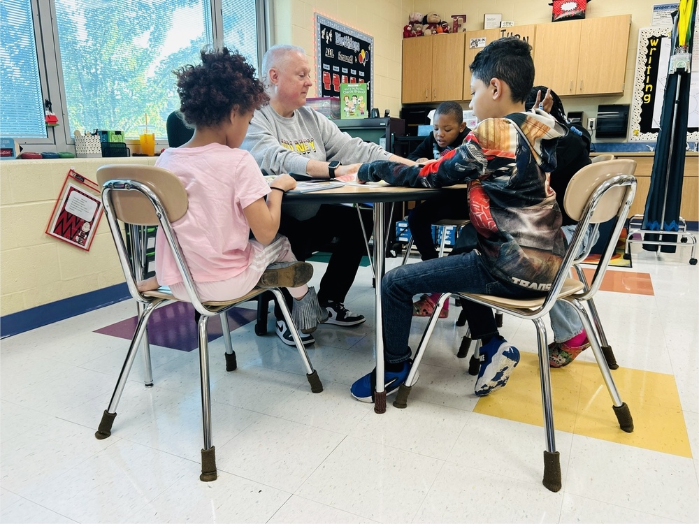 male teacher sitting at table with elementary students 