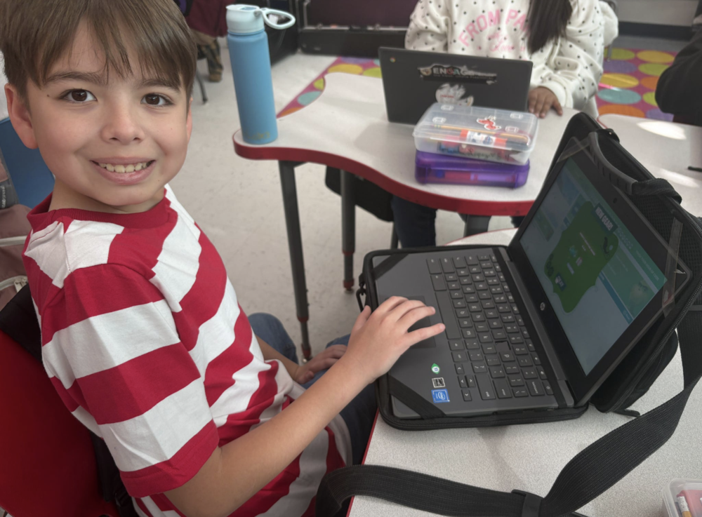 student smiling while showing his work on his computer