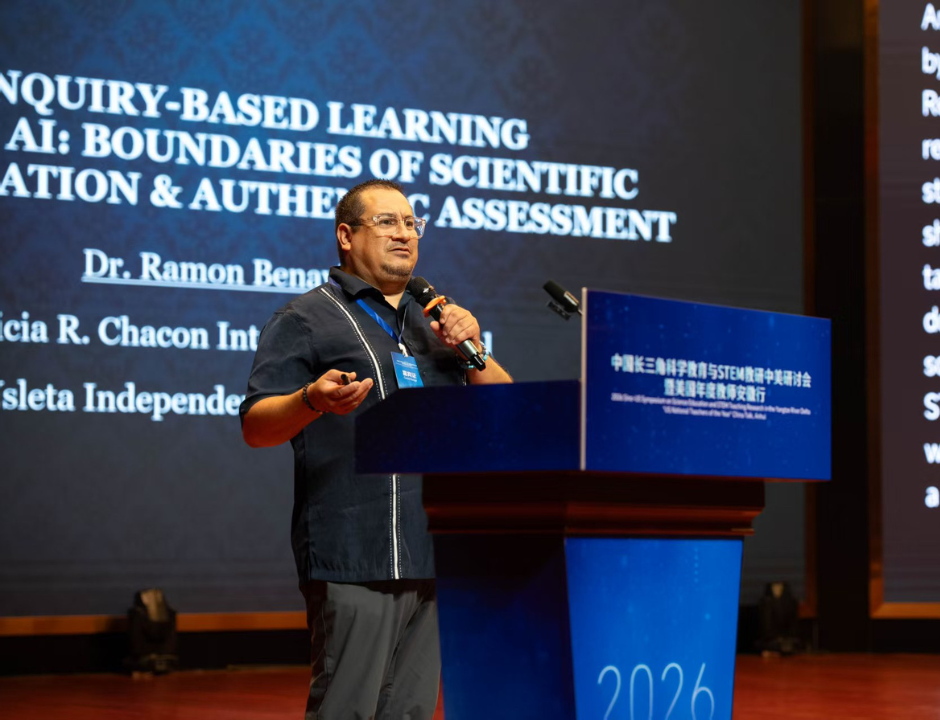 A man speaks at a podium during a conference, with a large screen behind him displaying a presentation titled Inquiry-Based Learning AI: Boundaries of Scientific Evaluation & Authentic Assessment.