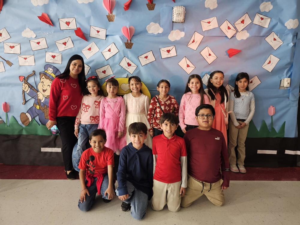Mrs. Alcocer's class poses in front of the backdrop with Valentine envelopes