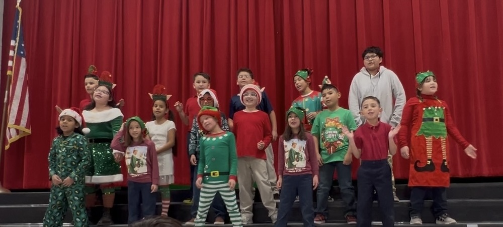 Ms. Reynoso's 3rd grade class sings on the steps of the stage in their holiday outfits of choice