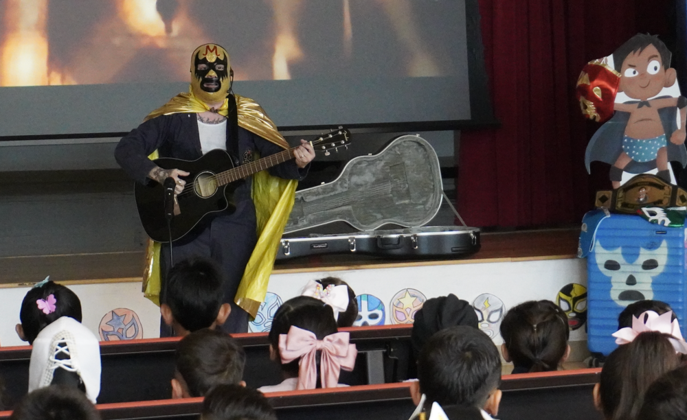 Author Miguel Briones wearing a luchador mask singing about his book.