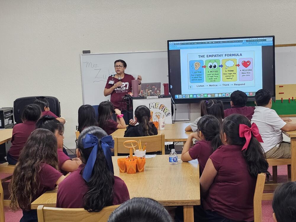 Mrs. Jordan teaches in front of the students in the library about Empathy. Students look on at the tables