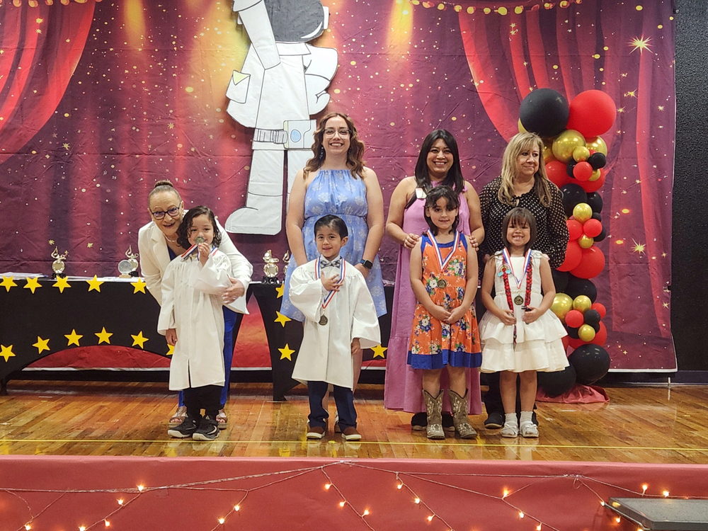 Pre-K and Kinder teachers posing with some of their students on stage after receiving some awards
