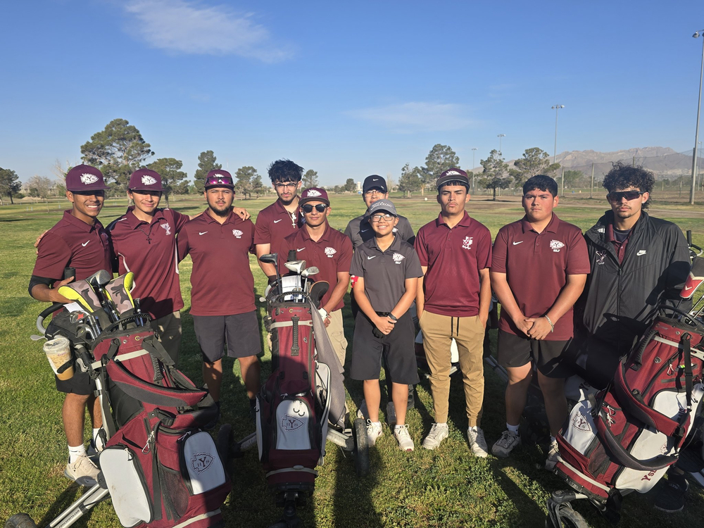 A group of nine Ysleta High School golf team members and their coaches posing together on a sunny golf course. The students wear maroon polo shirts with the YHS logo and caps, while some wear sunglasses. Two golf bags filled with clubs stand in the foreground. The team is smiling and looking at the camera, with green fairways, trees, and distant mountains in the background under a clear blue sky.