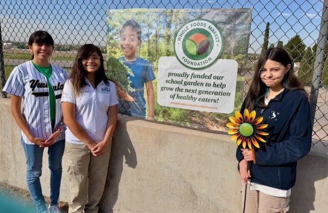 students at the garden on campus in front of the whole foods market sign