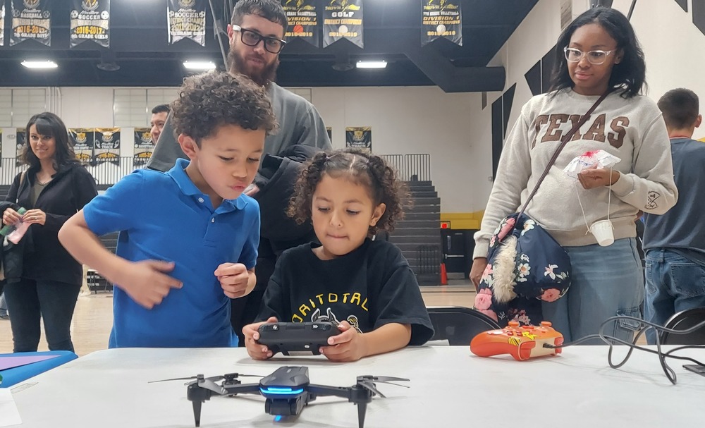A male and female student are turning on a remote control for a drone.