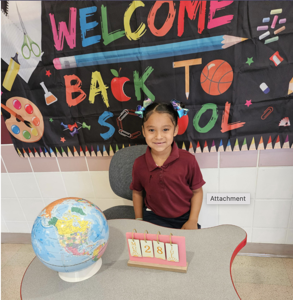 student sits at desk with a welcome back to school sign
