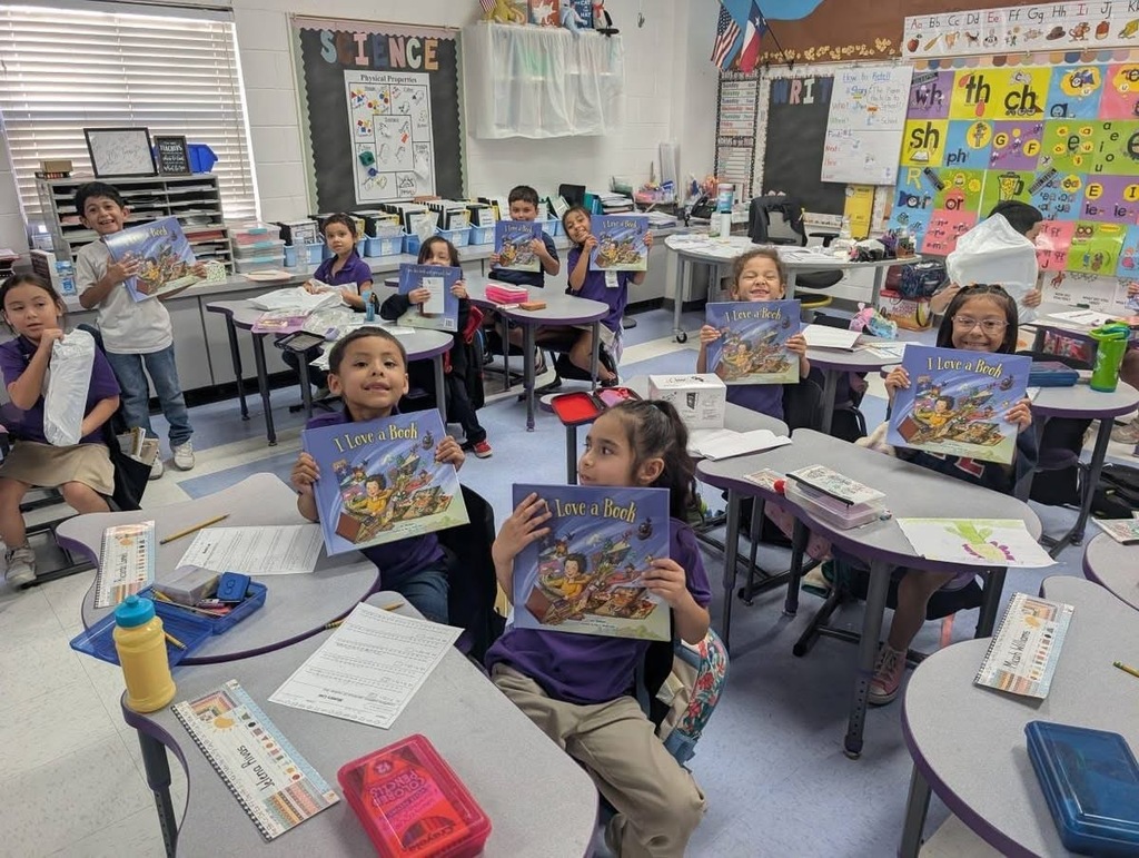 Students sitting down holding up their new books. 