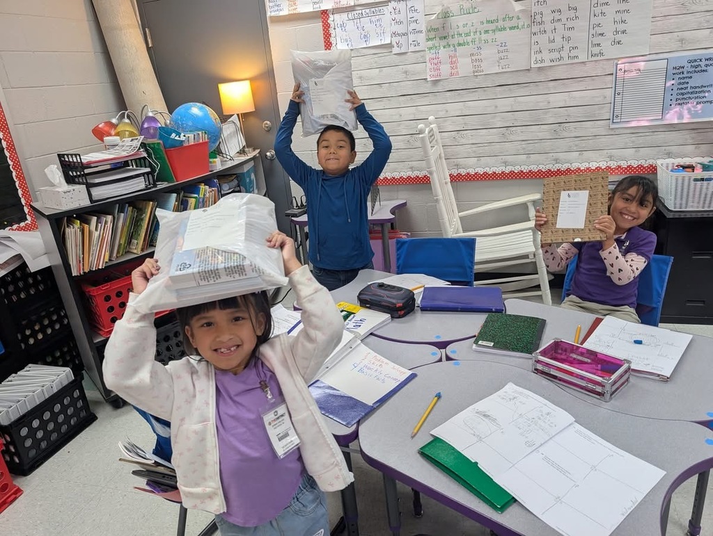 Students sitting down holding up their books. 
