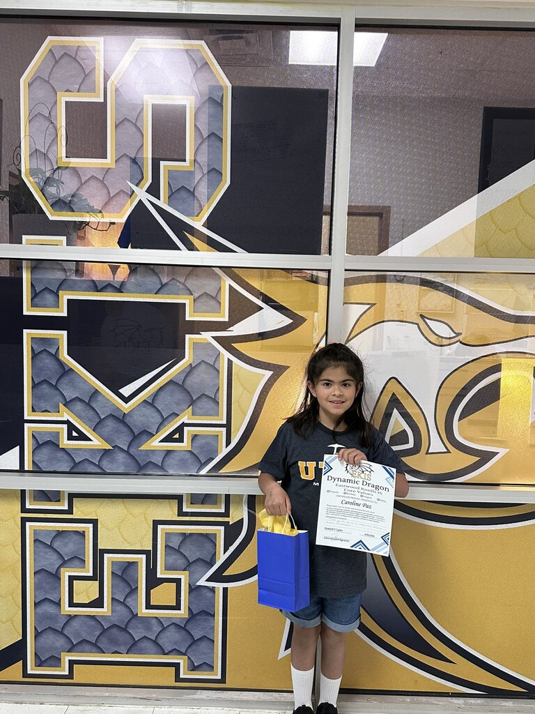 Photo of EKIS student Caroline, receiving a Dynamic Dragon Certificate for demonstrating core school values, Empathy, Kindness, Integrity, and Safety.