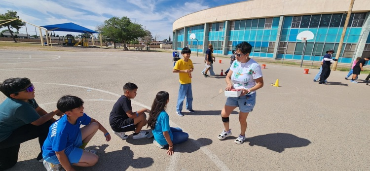 students sitting on a blacktop waiting to receive popsicle from adult PTO member