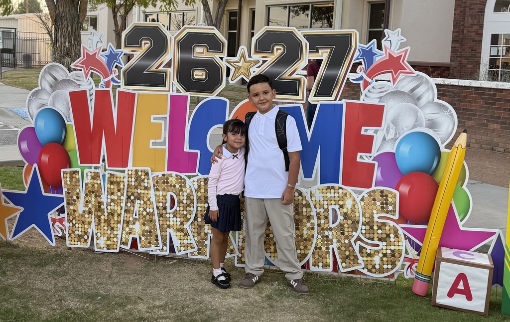 Students pose in front of a yard sign welcoming them back to school.